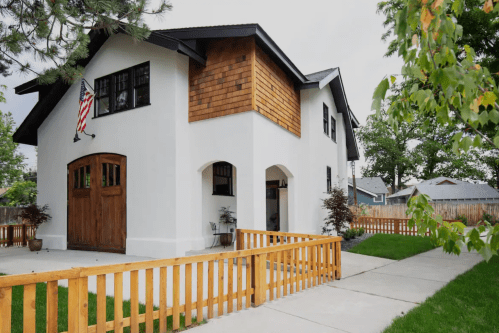 A modern two-story house with a wooden garage door, white exterior, and a wooden fence in front.